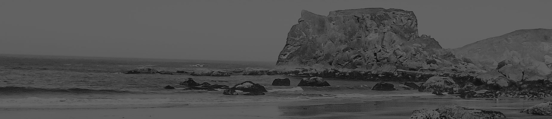 A grayscale sea stack rising from a beach at low tide, waves receding around it.